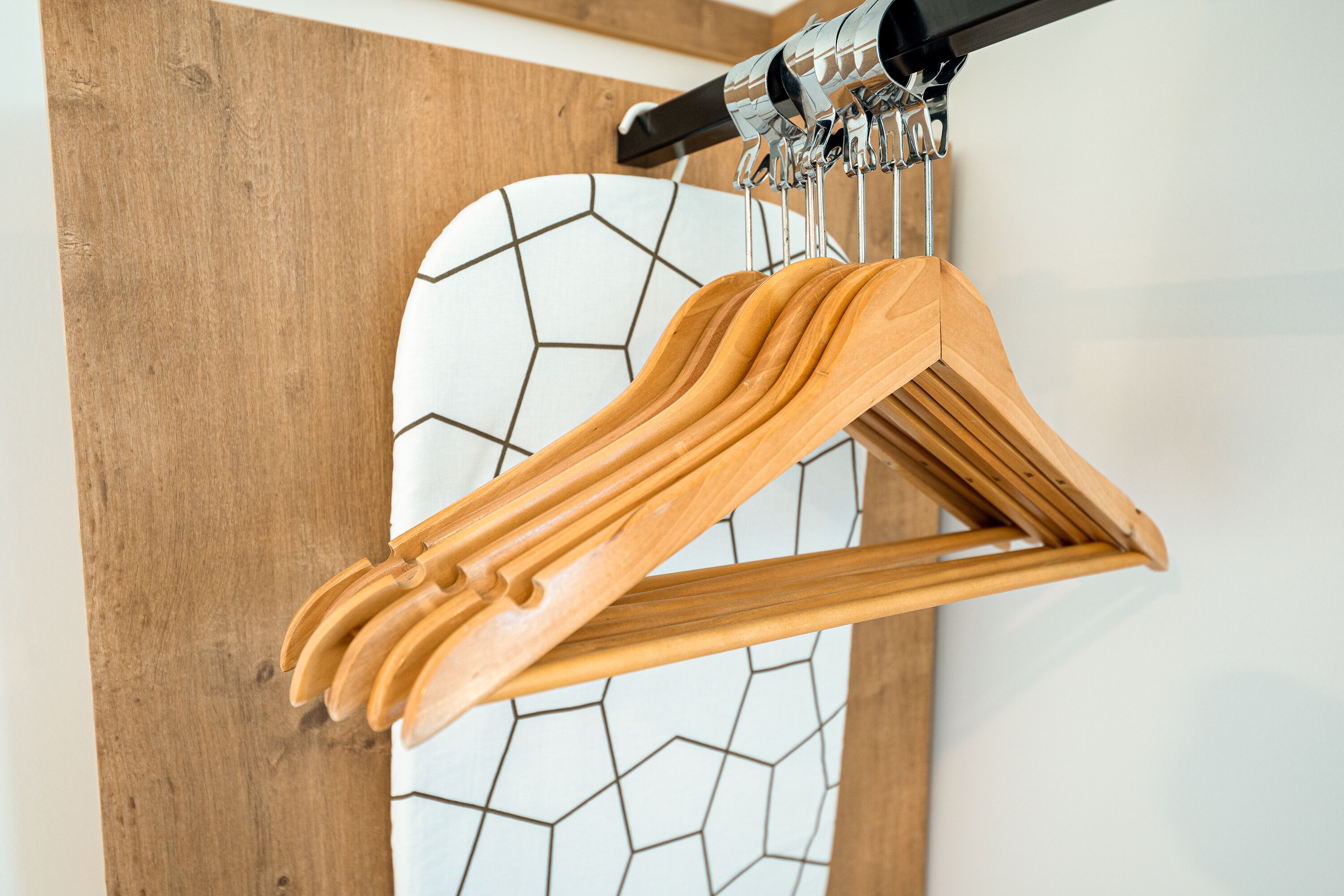 Suporte de madeira para cabides com vários cabides em frente a uma parede com padrão de azulejos geométricos.