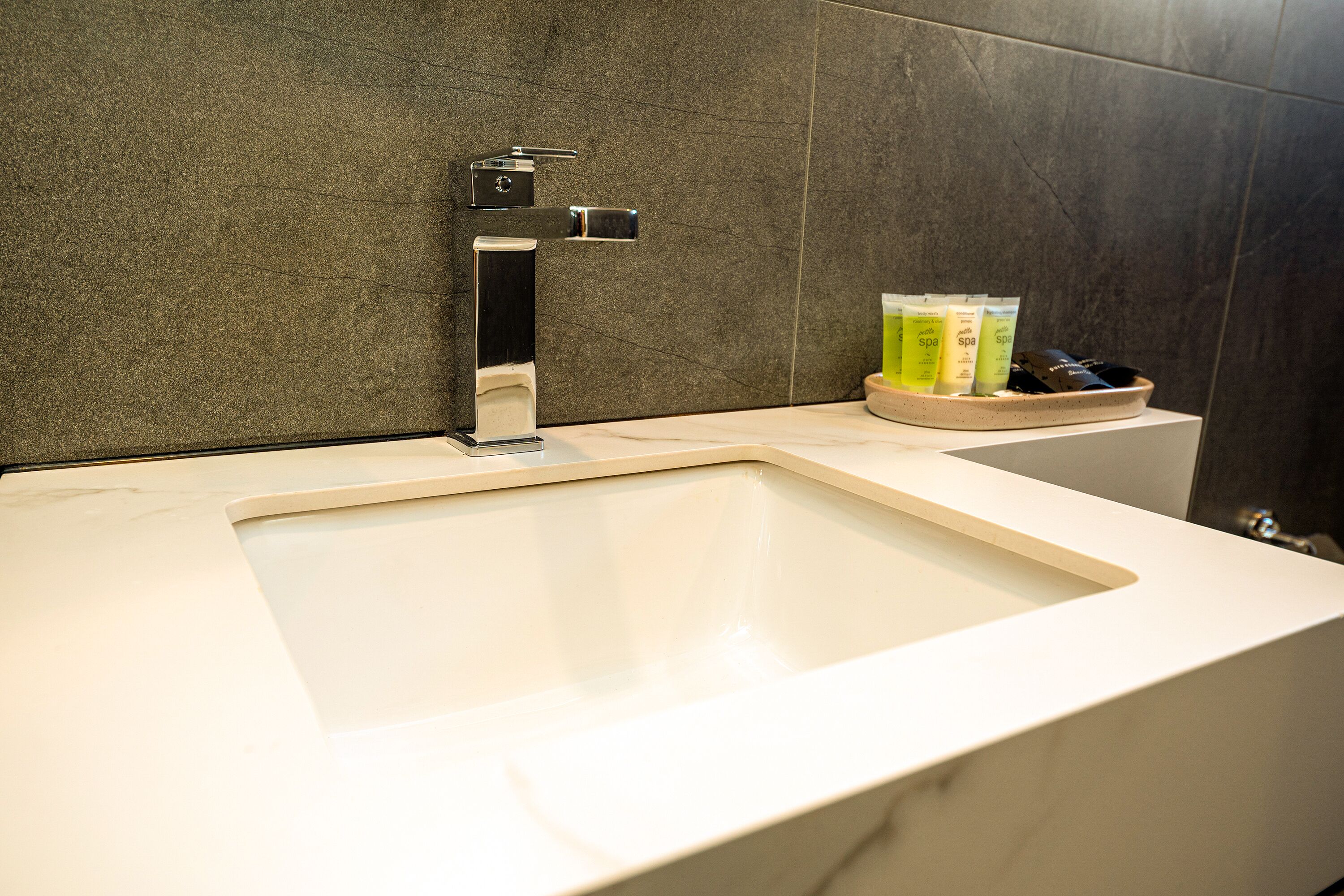 Un baño moderno con un lavamanos blanco, un grifo cromado y productos de spa sobre una bandeja de madera.