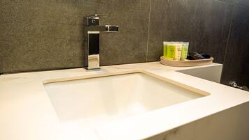 Un baño moderno con un lavamanos blanco, un grifo cromado y productos de spa sobre una bandeja de madera.