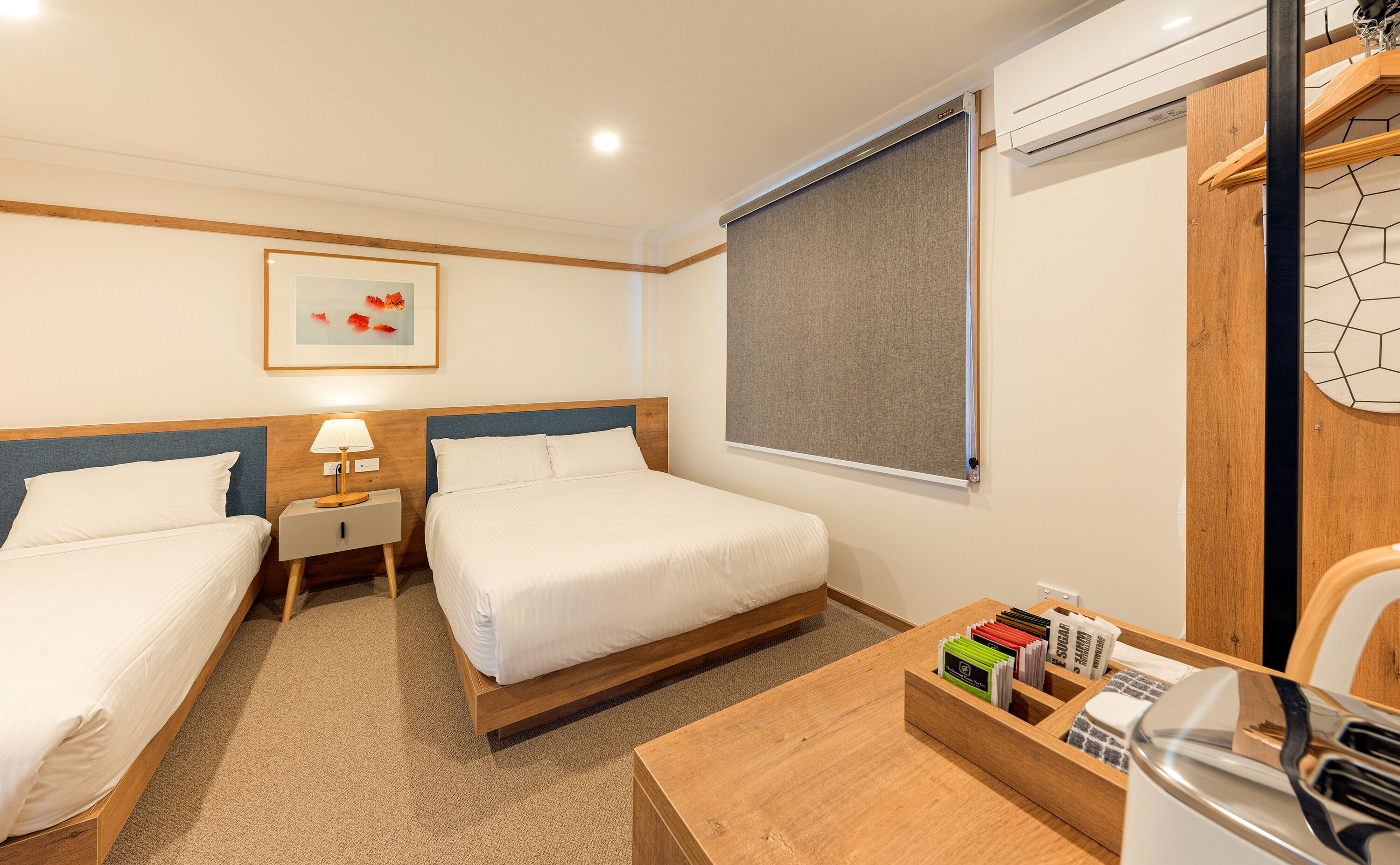 Habitación de hotel con dos camas, una mesita de noche con lámpara, un escritorio de madera con bandeja de artículos de aseo y una ventana con vistas al exterior.