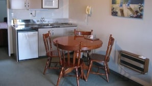 A compact kitchen with a microwave, sink, and a dining area with wooden chairs. - Blue Dolphin Motel (Timaru)