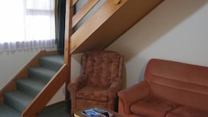 A staircase with wooden railings leading to an upper floor, a patterned armchair, and a red sofa in a room with a window. - Blue Dolphin Motel (Timaru)