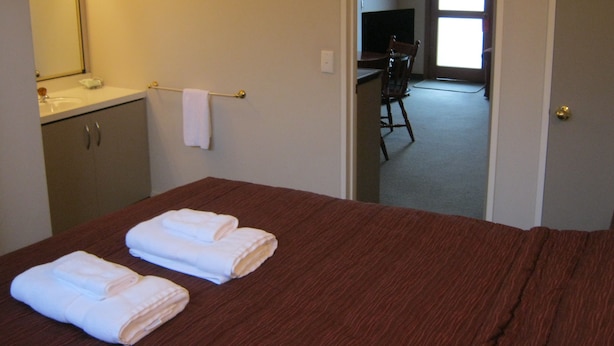 A hotel room with a bed, a desk, and a television in the adjacent room. - Blue Dolphin Motel (Timaru)
