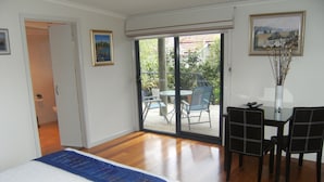 Un dormitorio con cama, escritorio y silla, un balcón con mesa y sillas, y un cuadro en la pared.