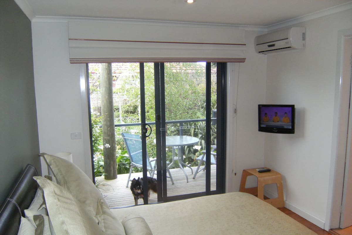 Un dormitorio con cama, televisión y balcón con mesa y sillas.