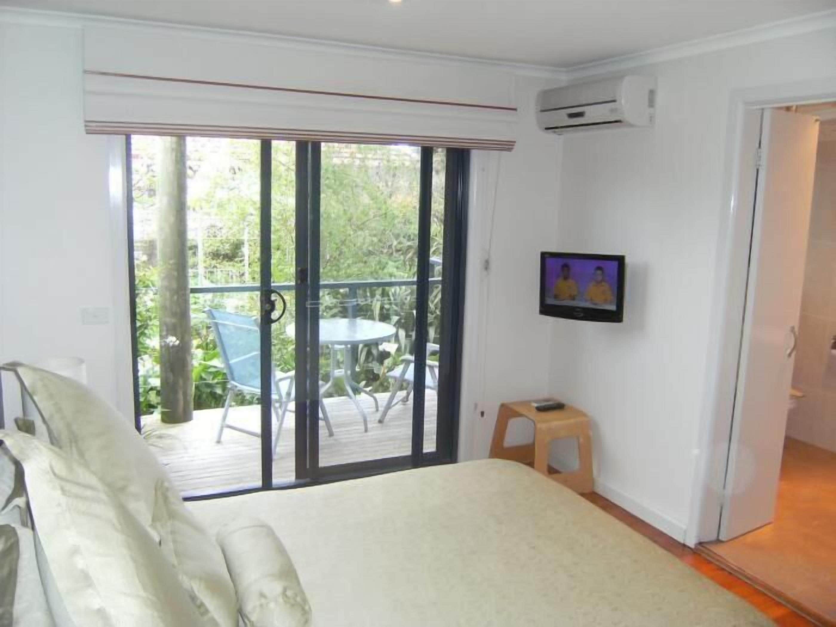 A bedroom with a bed, a TV, and a balcony with chairs.