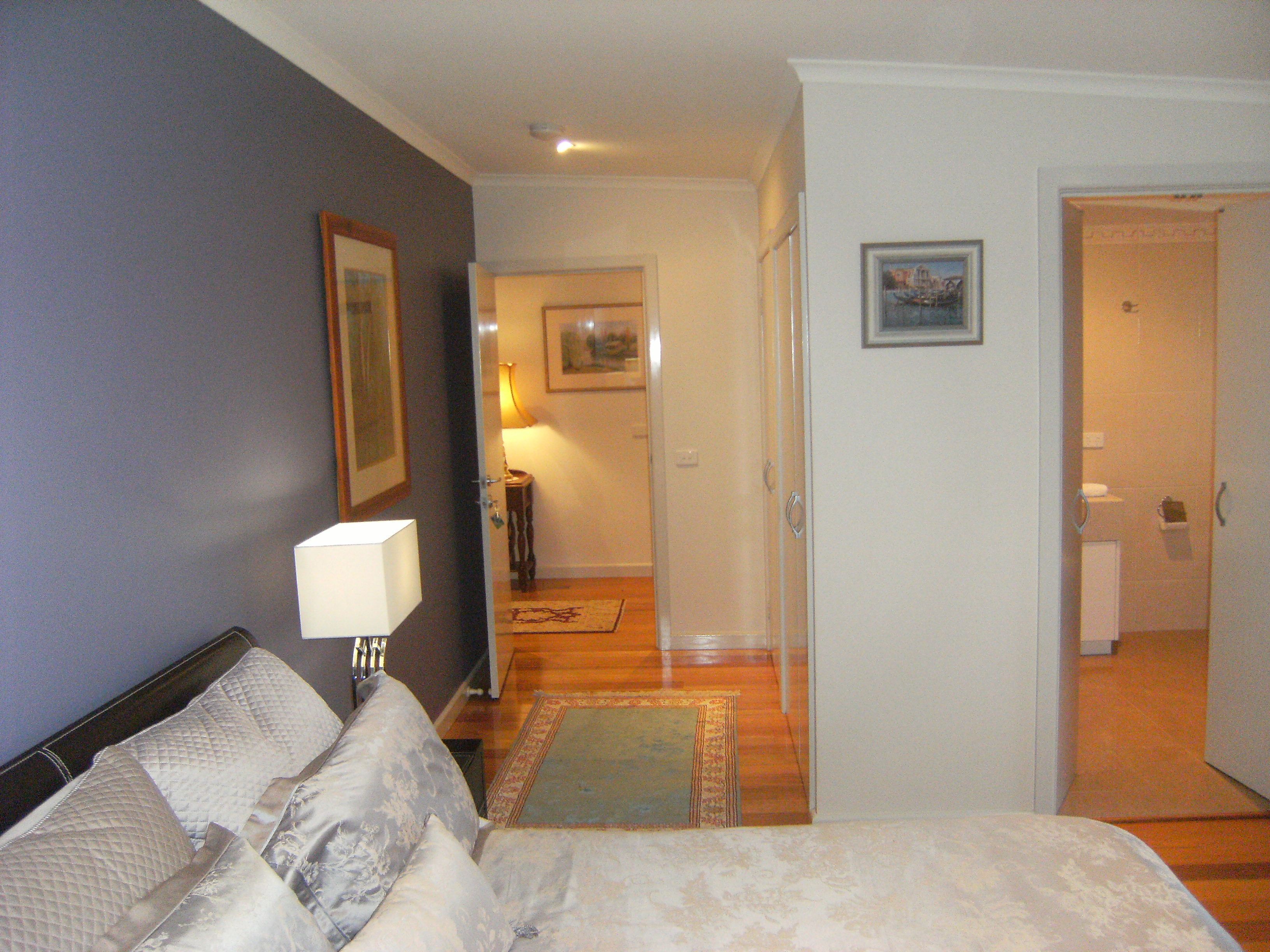 A bedroom with a bed, a nightstand, a lamp, and a door leading to a bathroom.