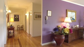 Un pasillo con suelo de madera, pared morada y un mueble con una lámpara y flores.