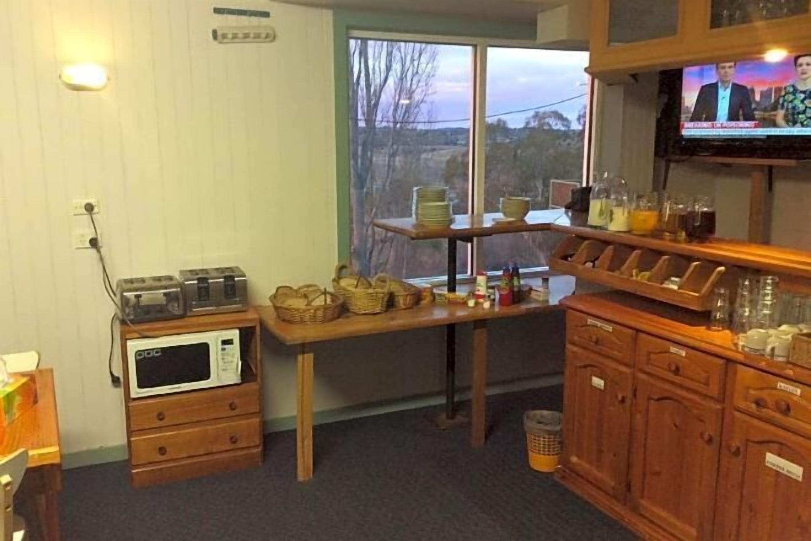 Una cocina con microondas, armarios de madera, una mesa con cestas y un televisor mostrando un noticiero.