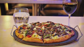 Une pizza sur un plateau en métal, accompagnée d’un verre d’eau et d’un verre de vin rouge, posés sur une table.