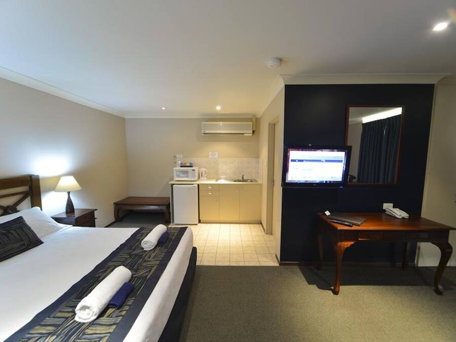 A hotel room with a bed, a desk, a small kitchenette, and a TV.