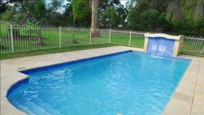 Une piscine rectangulaire aux parois bleues, entourée d’une clôture blanche, et agrémentée d’une petite cascade sur l’un des côtés.