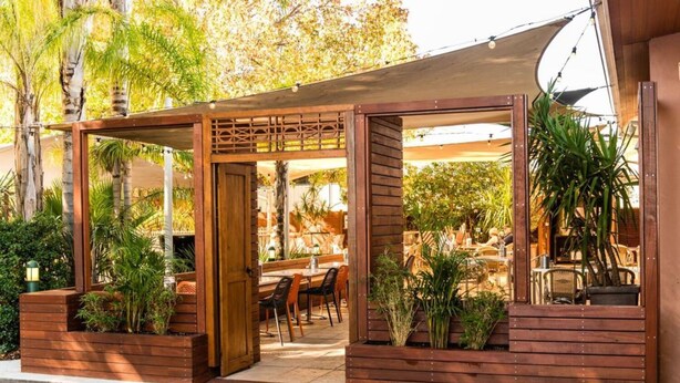 Un café en plein air doté de structures en bois, de tables, de chaises et de plantes en pot.