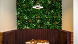 Un coin aménagé avec une table en bois, dressée pour le repas, un menu et un mur décoré de feuillage verdoyant.