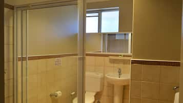 Un baño con cabina de ducha de vidrio, inodoro, lavabo y una ventana sobre el espejo.