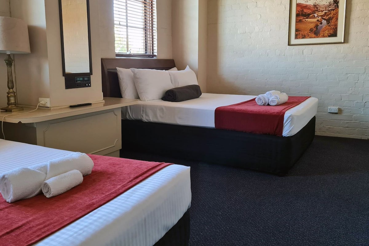 A hotel room with two beds, a desk, a lamp, and a painting on the wall.