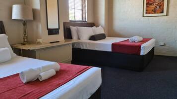 A hotel room with two beds, a desk, a lamp, and a painting on the wall.