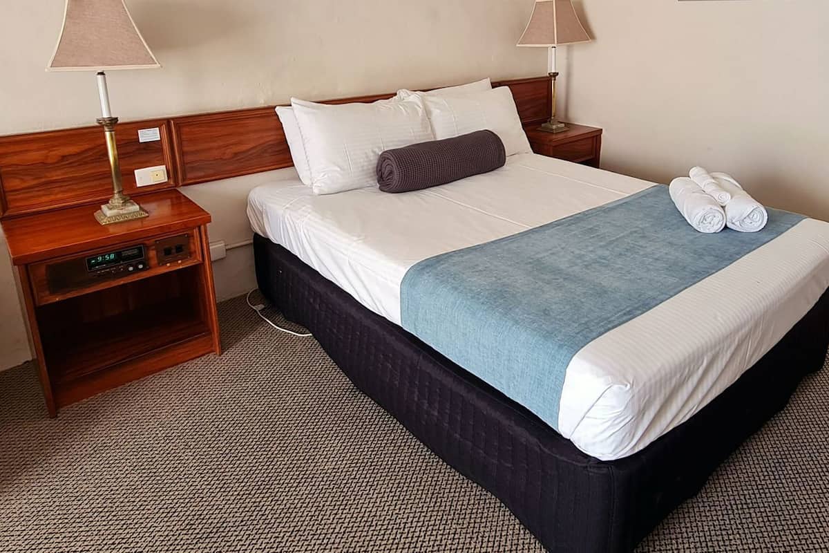 A hotel room with a bed, two bedside tables, a lamp, and a clock.
