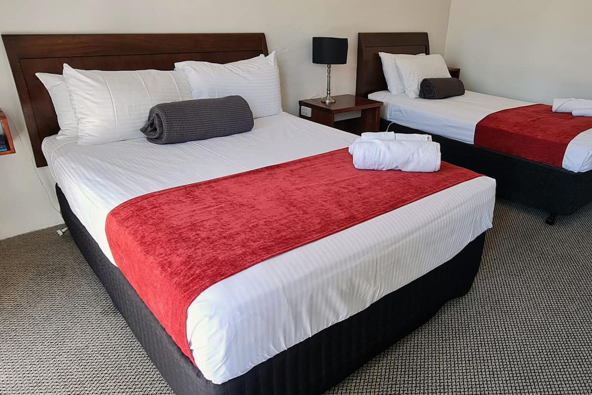 A hotel room with two beds, each with white linens and red throw blankets. There is a nightstand with a lamp between the beds.