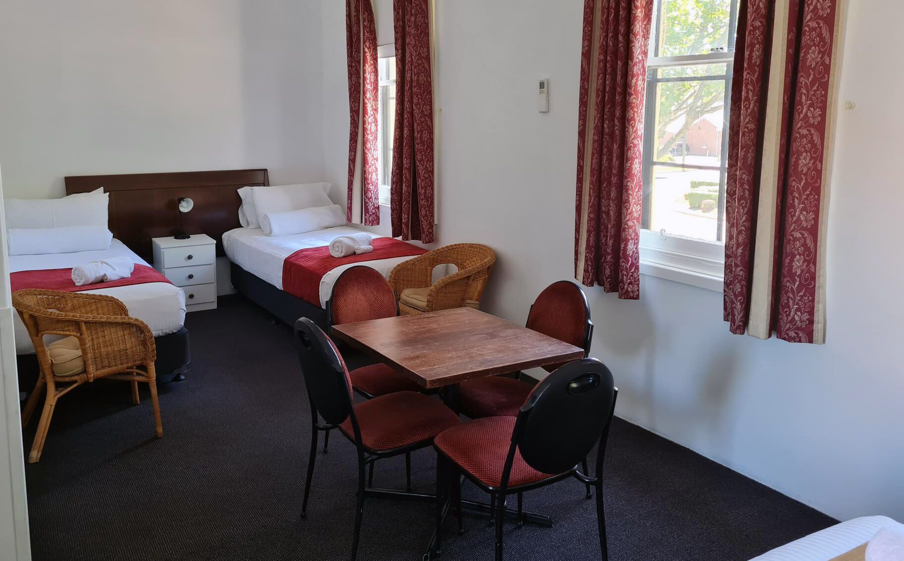 Quarto de hotel com duas camas, uma mesa de jantar e cadeiras. Há cortinas nas janelas.