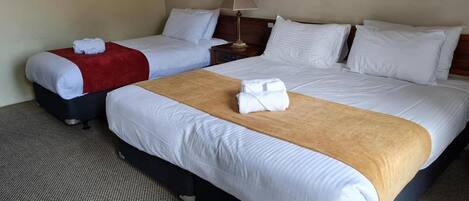 A hotel room with two beds, a red throw blanket on the left bed, a brown throw blanket on the right bed, and a lamp on the nightstand.