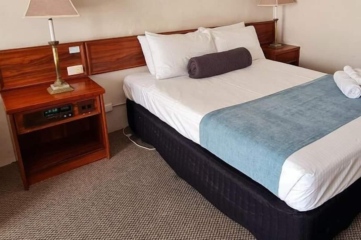 A hotel room with a bed, two bedside tables, a lamp, and a power outlet.