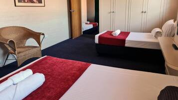 Une chambre d’hôtel avec deux lits, une chaise en osier, une armoire et un tableau encadré au mur.