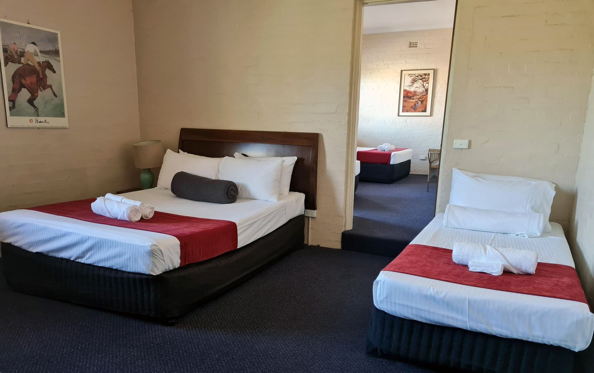 Une chambre d’hôtel avec deux lits, chacun recouvert d’une courtepointe rouge et blanche, dotée d’une tête de lit en bois et agrémentée de serviettes soigneusement pliées.