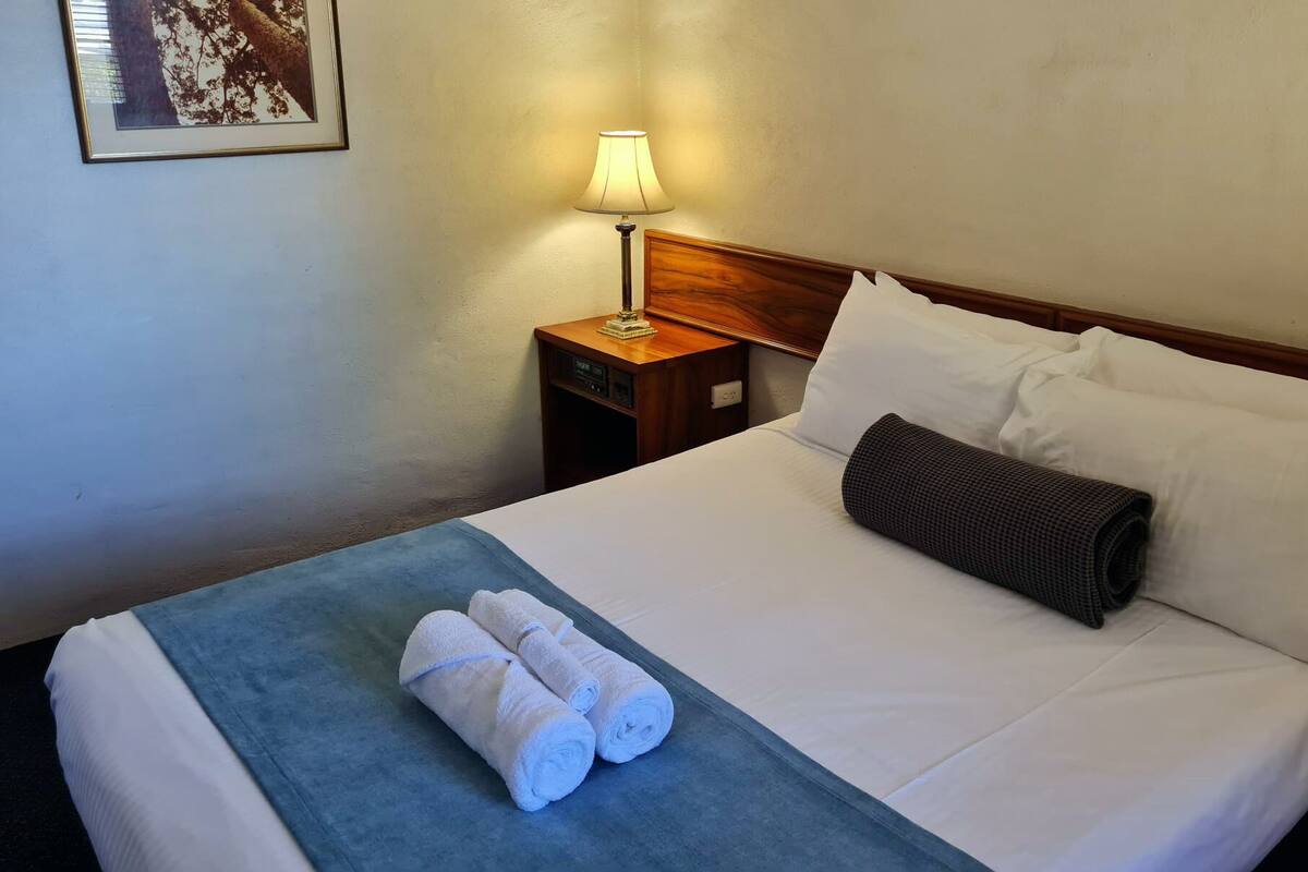 A neatly made bed with white linens, a blue blanket, and two rolled white towels.