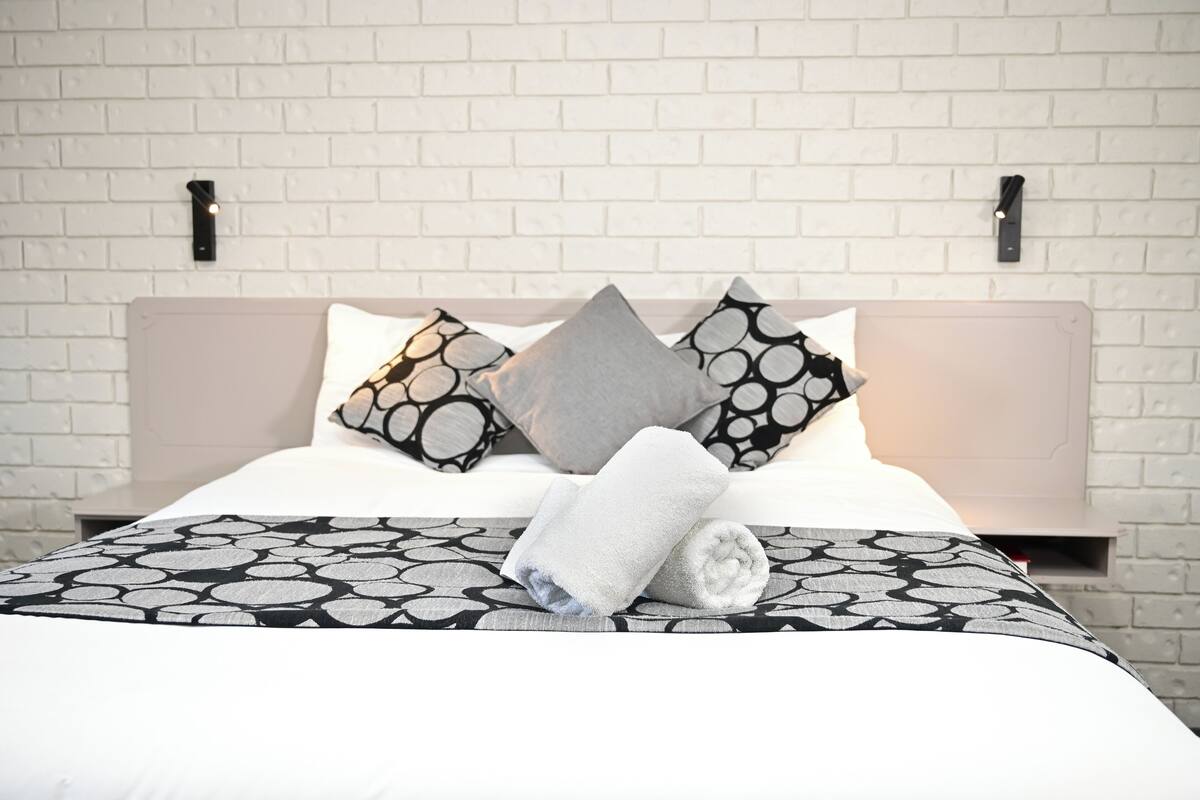 Een netjes opgemaakt bed met een bedsprei met een patroon, kussens met ronde motieven en een opgerolde handdoek op het bed.