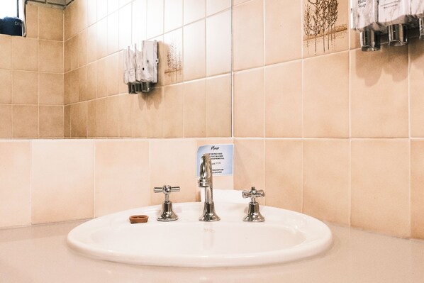 A bathroom sink with three faucets, a hand soap dispenser, and a sign above the sink.