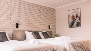 A hotel room with a brick-patterned wall, a bed with white bedding, and a framed picture of a plant. - Woomargama Village Hotel Motel (Woomargama)