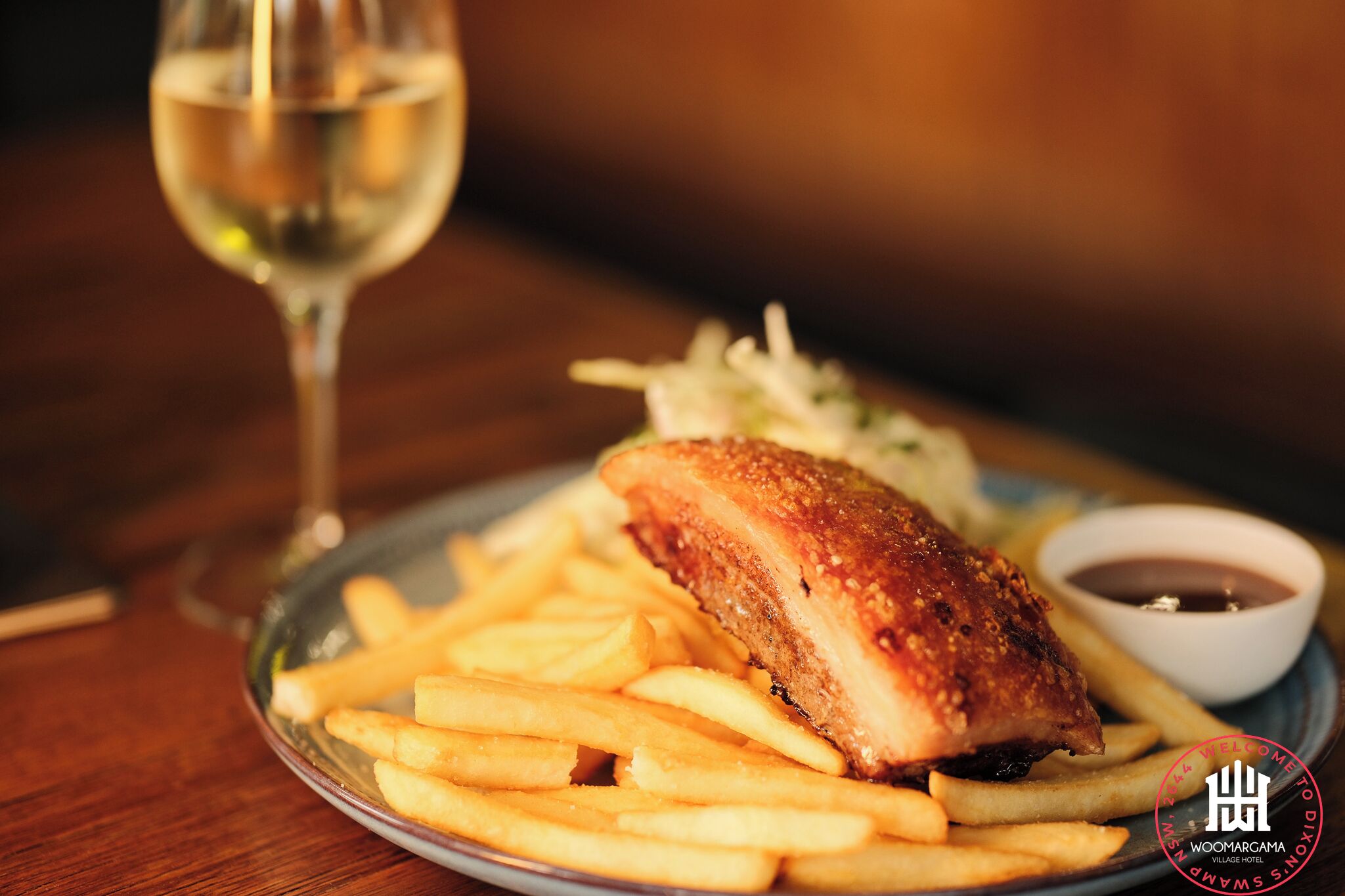 A plate with a breaded and fried item, possibly chicken, alongside French fries and a small bowl of sauce, with a glass of white wine on the side.