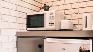A microwave on a countertop with a brick wall in the background. - Woomargama Village Hotel Motel (Woomargama)