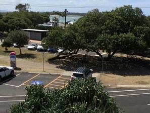 Un estacionamiento con varios autos, un edificio y un árbol grande.
