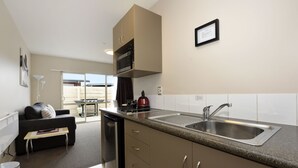 A compact kitchen with a sink, microwave, and cabinets. There is a dining area with a table and chairs, and a sofa in the background. - 171 On High Motel (Blenheim)