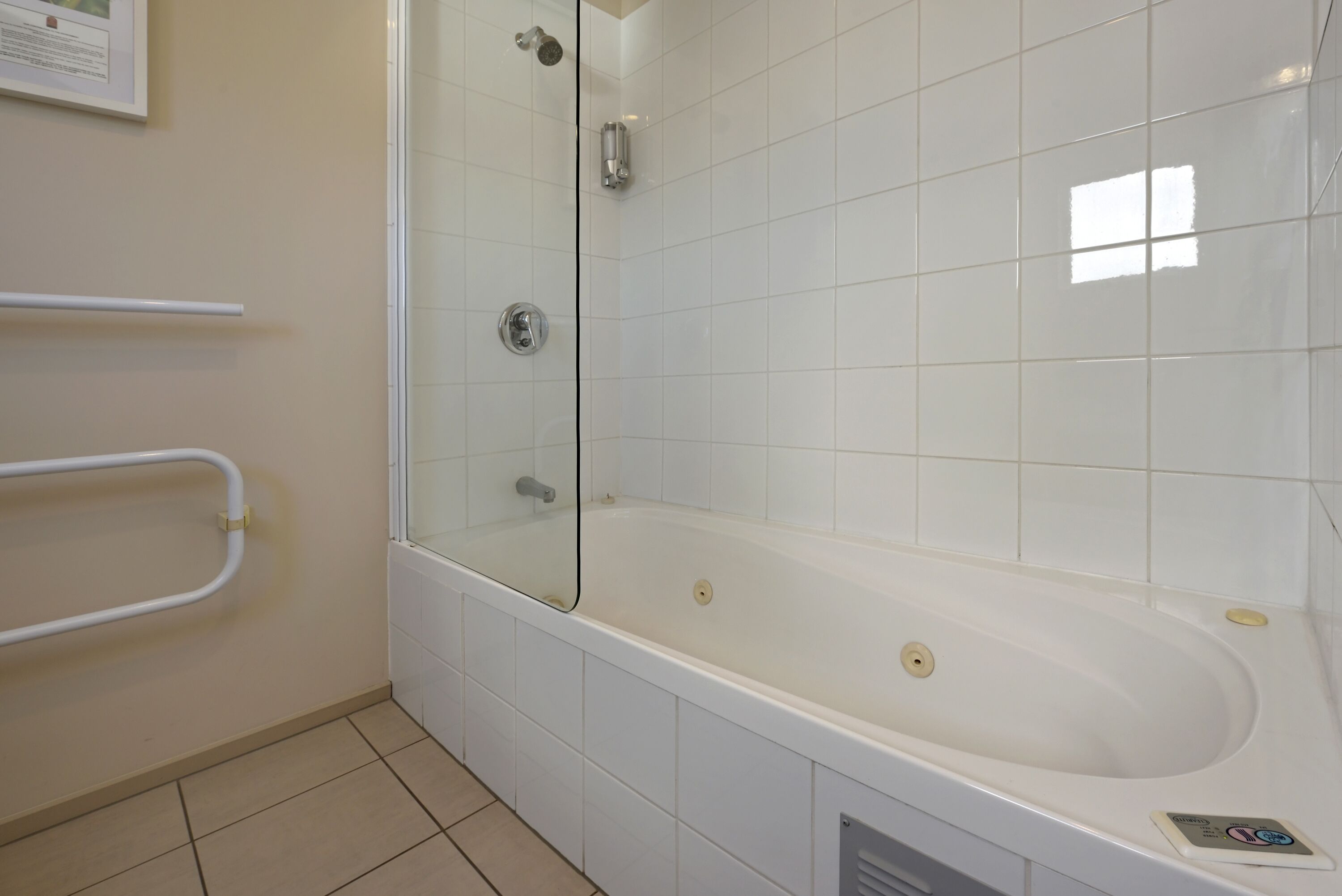 A bathroom with a glass-enclosed shower, a white bathtub, and a handrail.