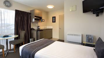 A hotel room with a bed, a desk, a chair, a microwave, a sink, and a television.