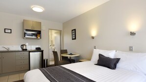 A hotel room with a bed, a desk with a microwave, a chair, and a small table. - 171 On High Motel (Blenheim)