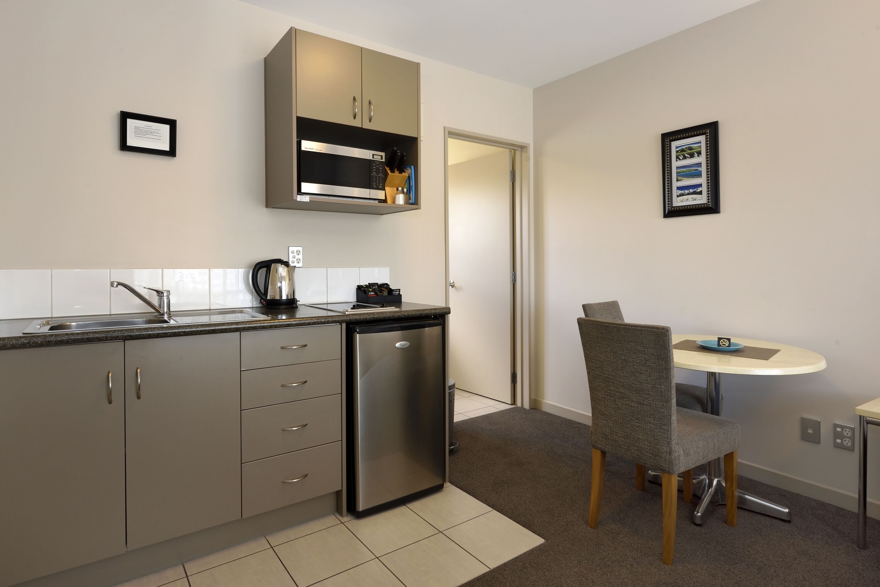 A compact kitchen with a built-in microwave, a coffee maker, and a small refrigerator. There is a dining area with a round table and a single chair.