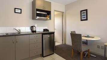 A compact kitchen with a built-in microwave, a coffee maker, and a small refrigerator. There is a dining area with a round table and a single chair.