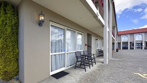 A covered outdoor seating area with tables and chairs, a potted plant, and a building with large windows and a red roof. - 171 On High Motel (Blenheim)