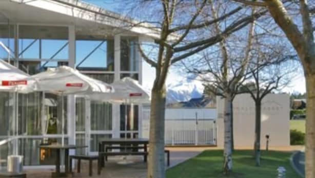 A modern building with a glass facade, outdoor seating area, and a view of a mountain range.
