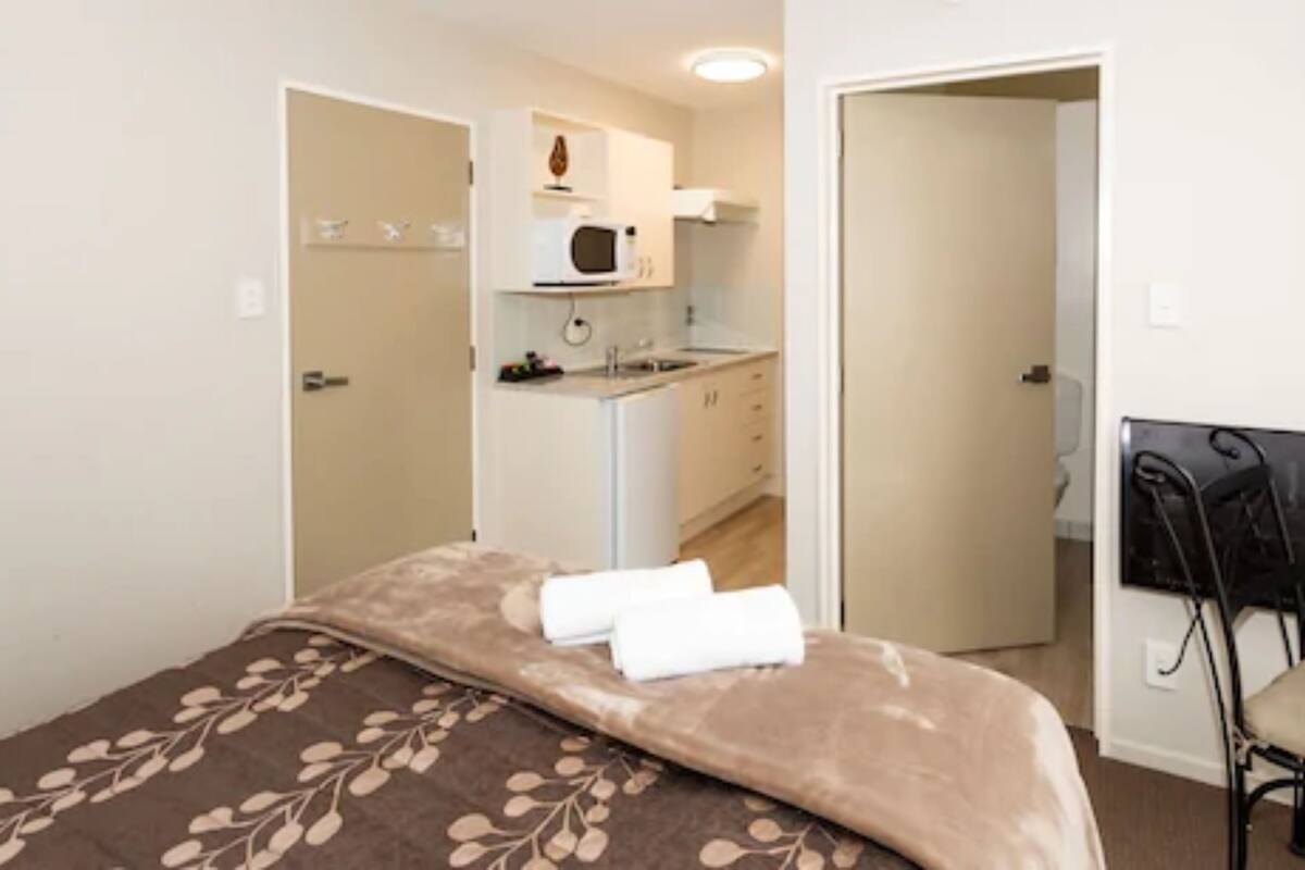 Ein Schlafzimmer mit einem Bett, einem Sessel und einer Küchenzeile im Hintergrund.