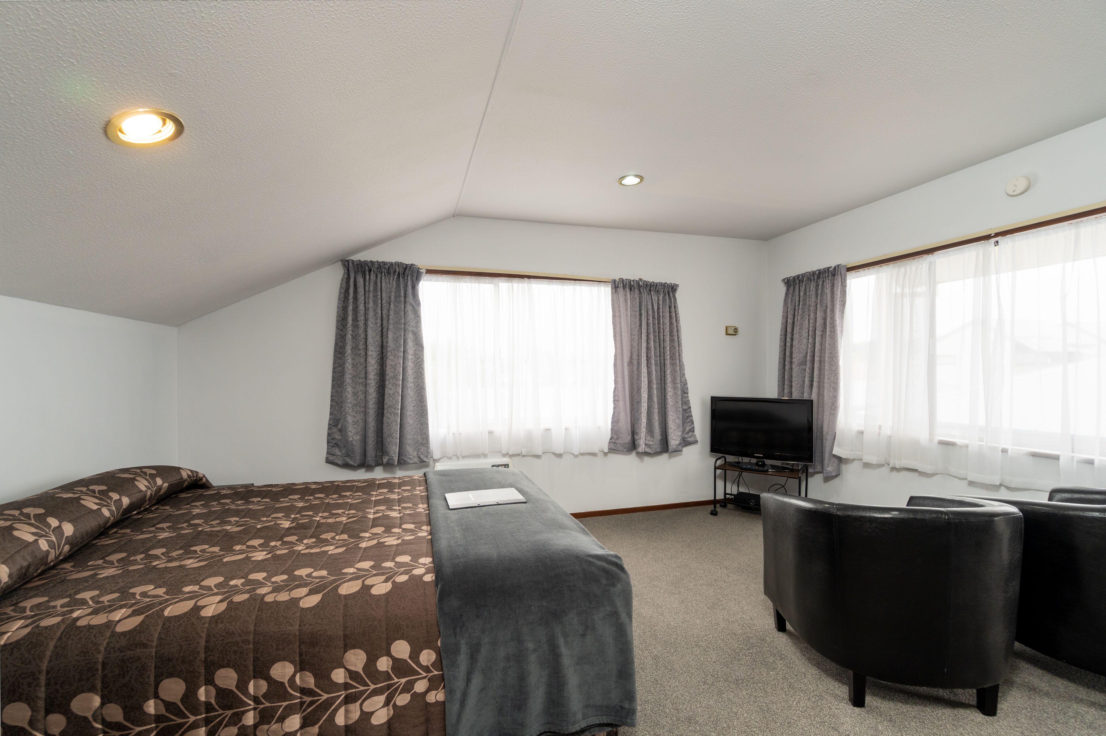 A hotel room with a bed, a desk, a TV, and two chairs.