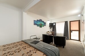A hotel room with a bed, a desk, a chair, a TV, and a painting on the wall.