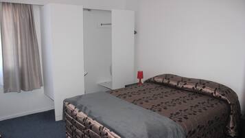 Um quarto com cama, guarda-roupa, luminária vermelha e janela com cortinas.