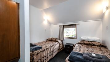 Una habitación pequeña y funcional con dos camas individuales, un armario de madera, un escritorio pequeño y una ventana con vistas al exterior.
