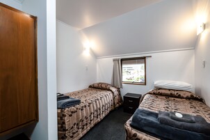 Una habitación pequeña y funcional con dos camas individuales, un armario de madera, un escritorio pequeño y una ventana con vistas al exterior.