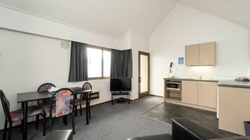 A compact living space with a dining area, a sofa, a television, a kitchenette, and a door leading to another room.